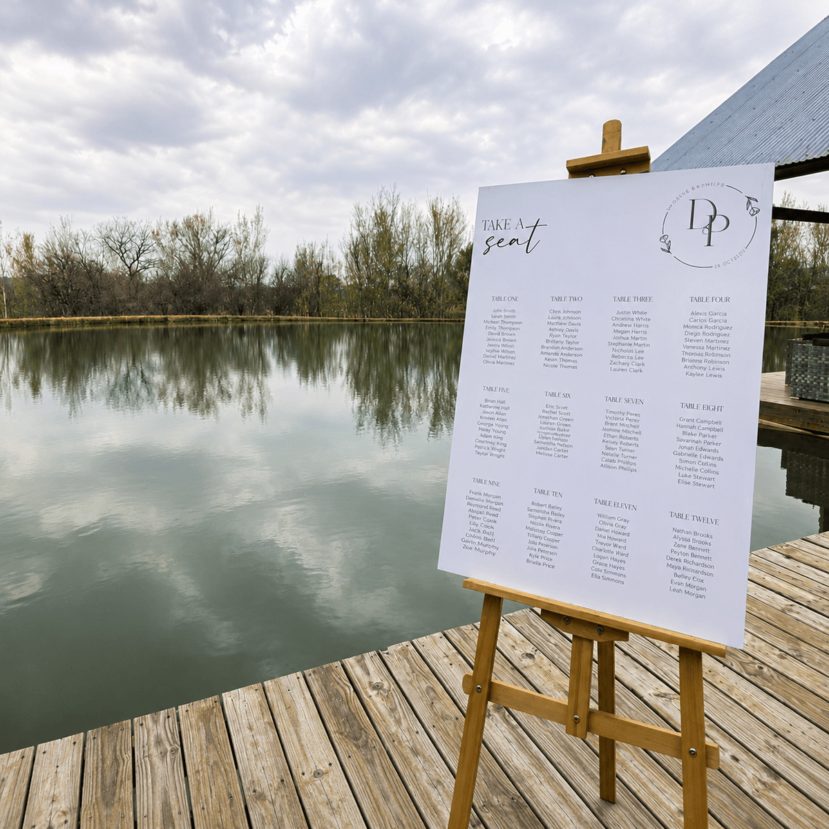 Seating chart on an easel by a lake reading 'Take a seat'